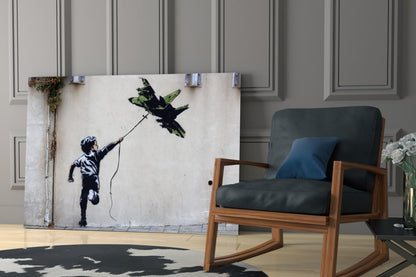 Banksy-style glass art depicting child flying kite displayed on living room wall beside wooden chair.