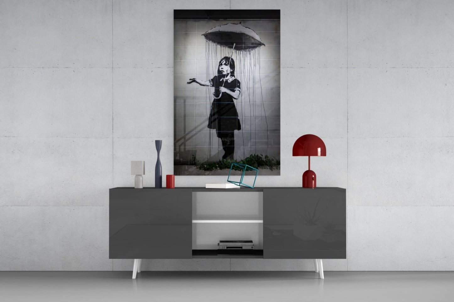 Black and white glass art print of girl with umbrella displayed on gray media console with red lamp and decorative objects.