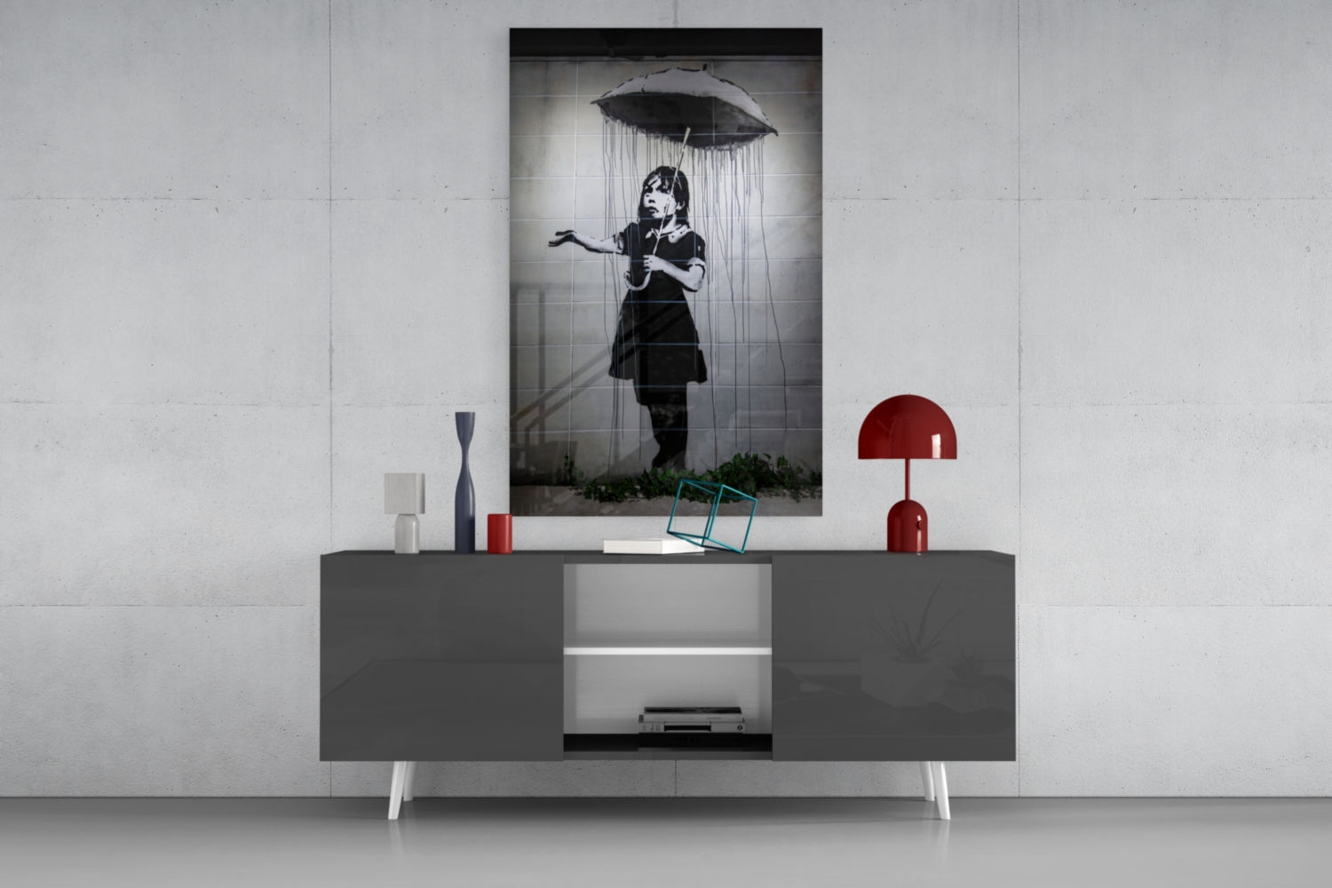Black and white glass art print of girl with umbrella displayed on gray media console with red lamp and decorative objects.