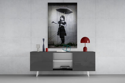 Black and white glass art print of girl with umbrella displayed on gray media console with red lamp and decorative objects.