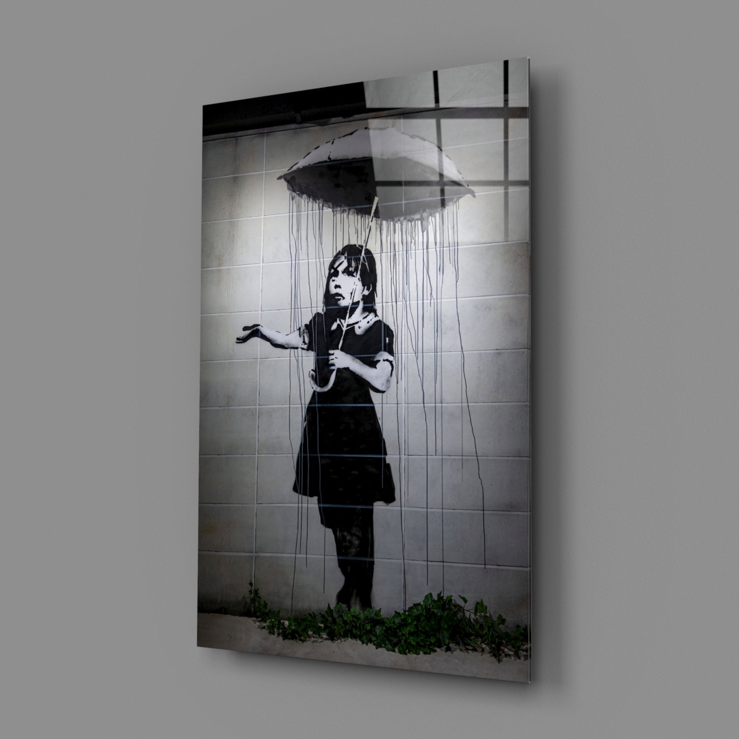 Glass art print mounted on gray wall showing black and white stencil of child with umbrella under raining eye.