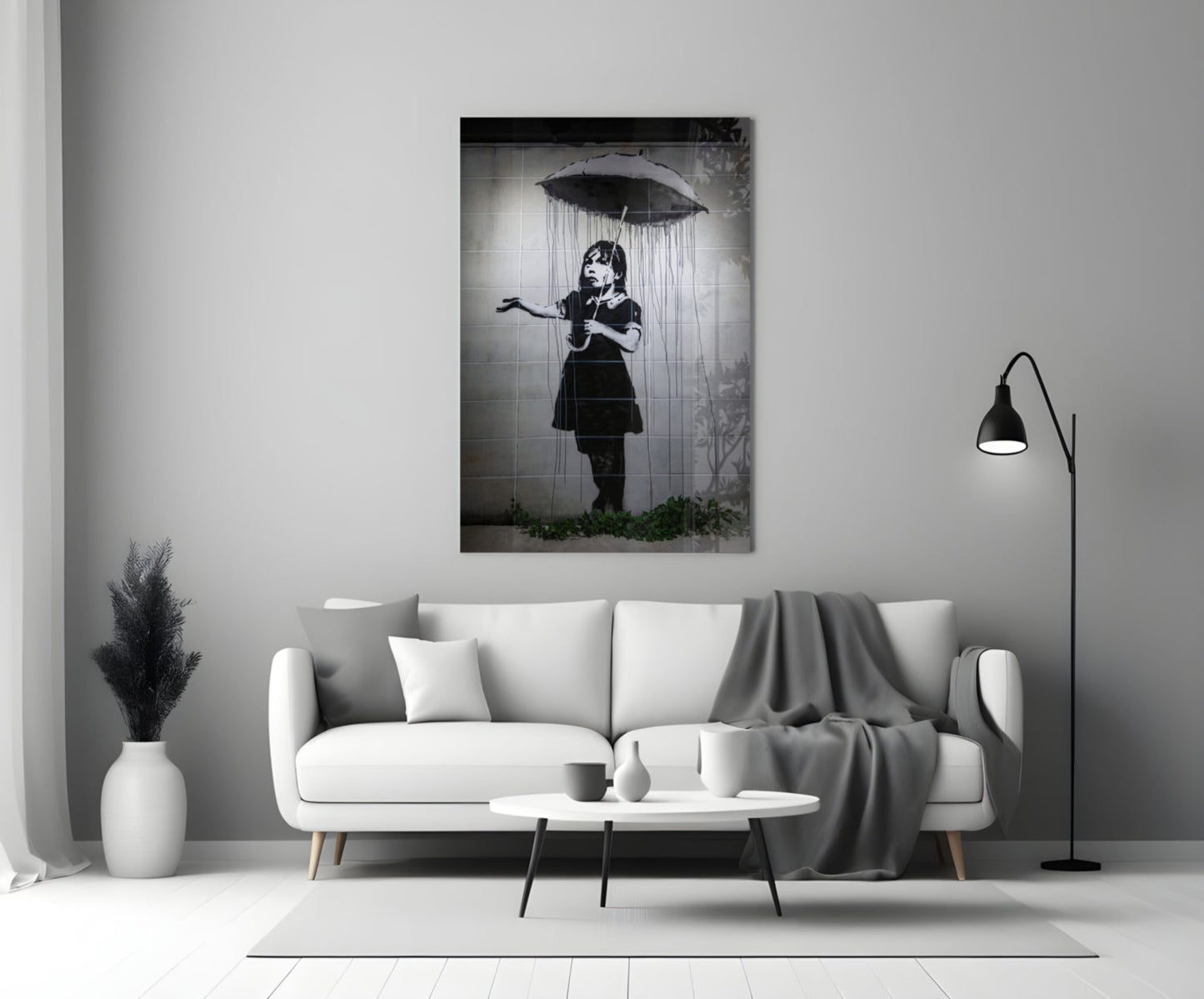 Black and white glass art depicting a child holding an umbrella beneath falling rain, displayed above a white sofa in a minimalist living room.