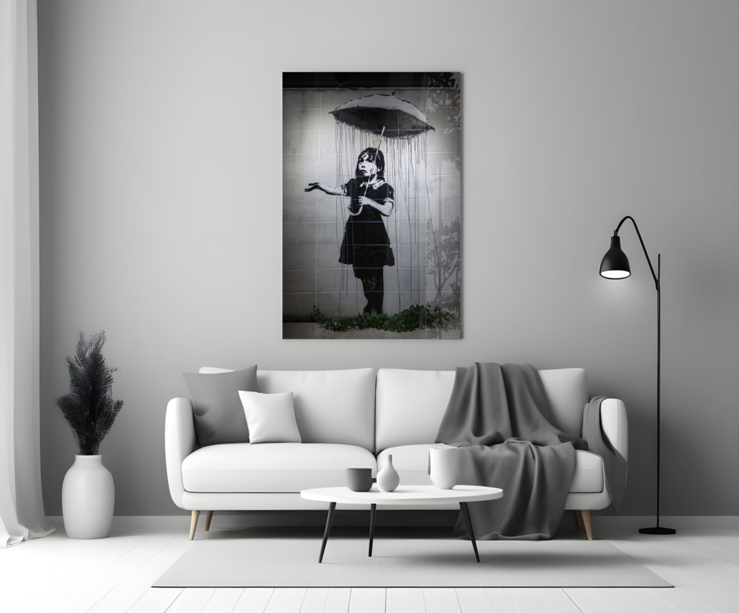 Black and white glass art depicting a child holding an umbrella beneath falling rain, displayed above a white sofa in a minimalist living room.
