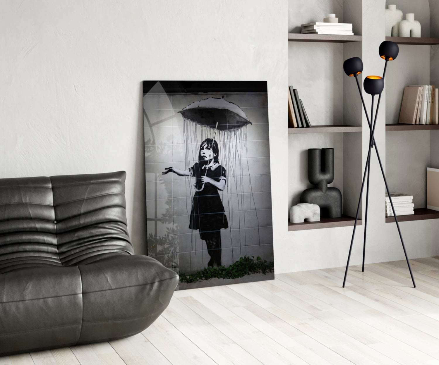 Black and white glass art depicting a child holding an umbrella in rain, displayed in a modern living room with grey furniture and wooden shelving.