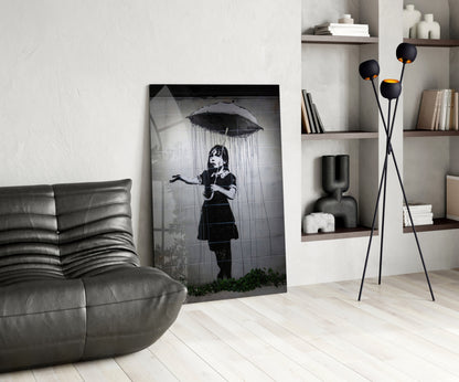 Black and white glass art depicting a child holding an umbrella in rain, displayed in a modern living room with grey furniture and wooden shelving.