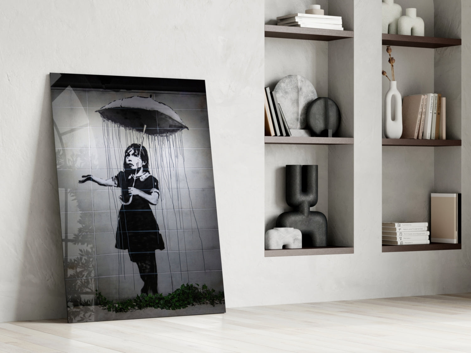 Black and white glass art leaning against white wall beside built-in shelving with decorative objects and books.