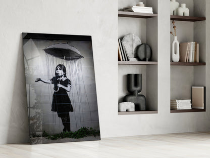 Black and white glass art leaning against white wall beside built-in shelving with decorative objects and books.