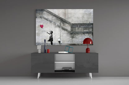 Banksy-style glass art depicting silhouetted girl reaching for red heart balloon displayed above modern media console in minimalist interior.