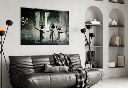 Dark glass art print depicting three stick figures with TV screens for heads against weathered green and gray background, hung above gray leather sofa in modern living room.