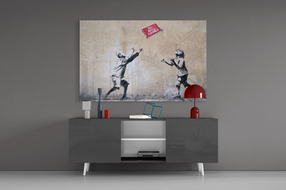 Banksy-style stenciled artwork displayed above gray media console showing two children reaching for red ball, with "NO BALL GAMES" sign visible.