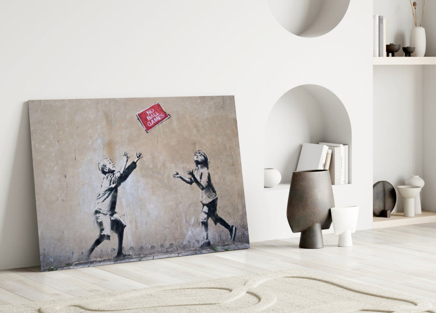 Banksy "No Ball Games" artwork displayed on floor against white wall with sculptural objects and built-in shelving.