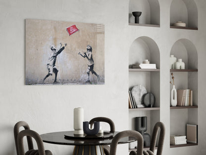 Banksy-style canvas artwork depicting two children reaching for a red "No Ball Games" sign, displayed above a black dining table in a modern interior.