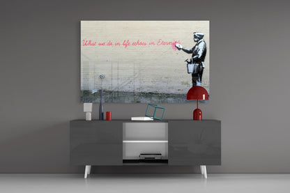 Banksy-style street art glass print mounted above gray media console displaying stenciled figure with red text quote and red decorative accessories.
