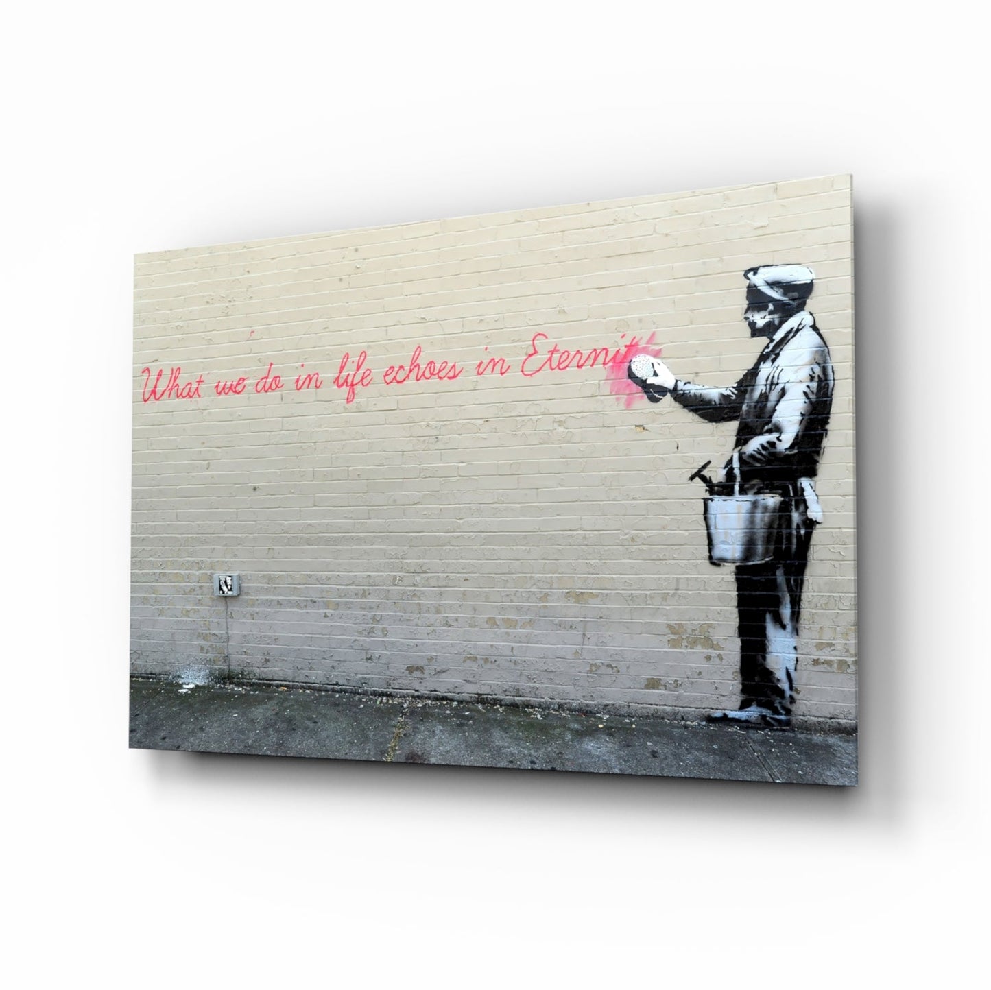 Glass art print displayed at an angle showing stenciled figure with bucket and pink handwritten text on wooden wall background.