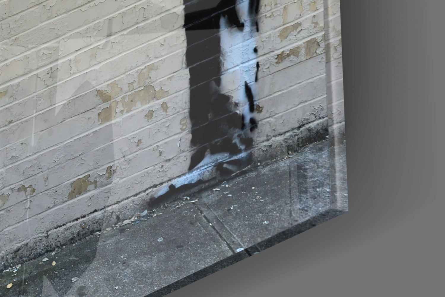Glass art piece leaning against white painted brick wall on concrete ground, showing reflection and shadow detail.