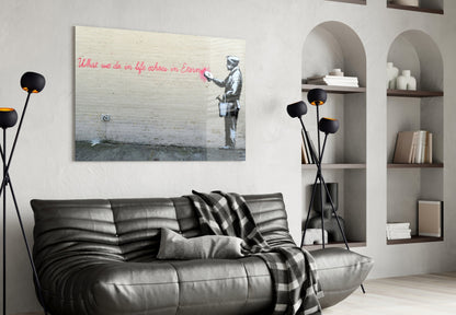 Banksy-style street art glass print hung above black leather sofa in modern living room with shelving and floor lamp.