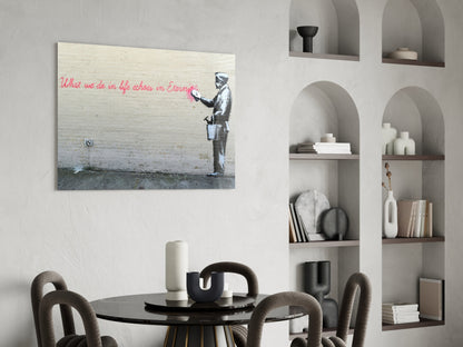 Glass art print featuring stenciled figure with pink handwritten text hung above round black dining table with grey chairs.