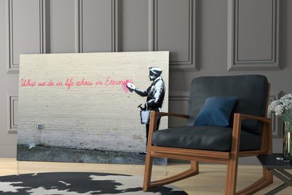 Glass art print of Banksy-style stencil figure with pink cursive text displayed on white brick wall beside wooden chair.