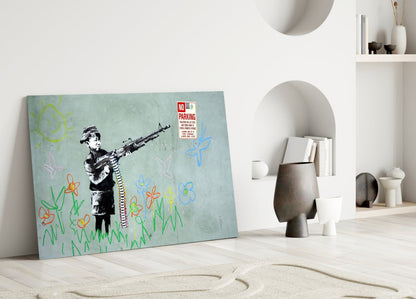 Glass art print leaning against white wall featuring stenciled child figure holding rifle with colorful childlike drawings of flowers and sun on pale blue background.