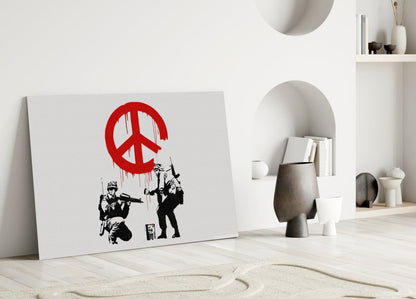 White canvas with red peace symbol and black stenciled soldiers leaning against white wall in minimalist interior setting.