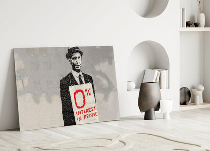 Canvas artwork leaning against white wall displaying stenciled figure in suit holding sign reading "0% INTEREST IN PEOPLE" in red text.