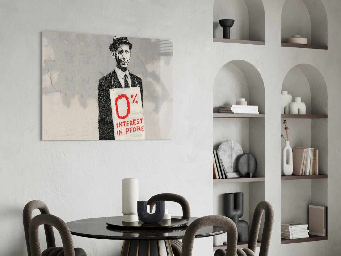Stenciled portrait of suited man holding red text sign reading "0% Interest in People" hung above dining table in modern interior.