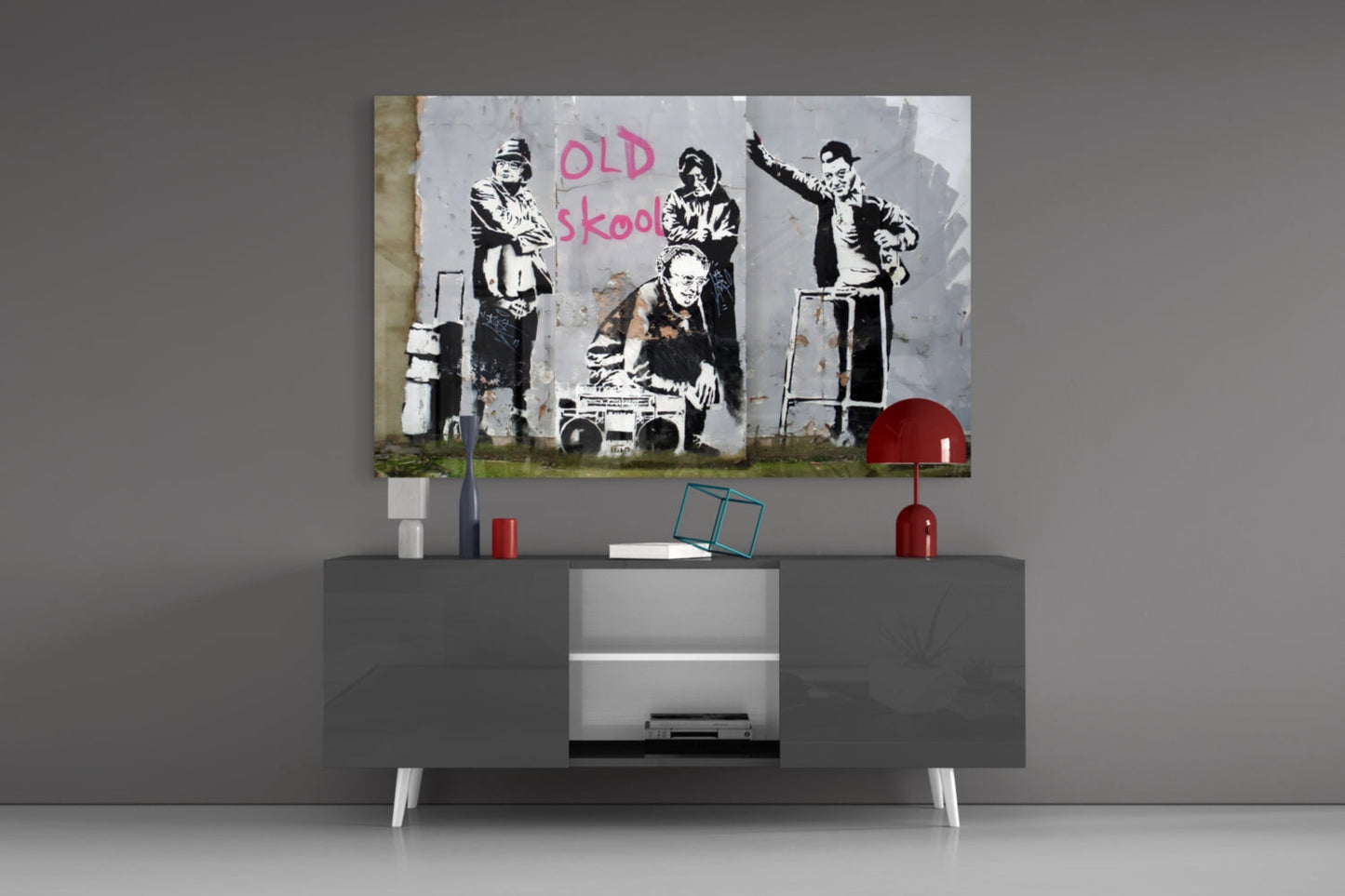 Banksy "Old Skool" stenciled street art print displayed on gray modern TV console with red accents and white legs.