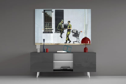 Soldier glass art depicting two military figures in camouflage exchanging a box beside a shopping cart, displayed above a modern gray media console.