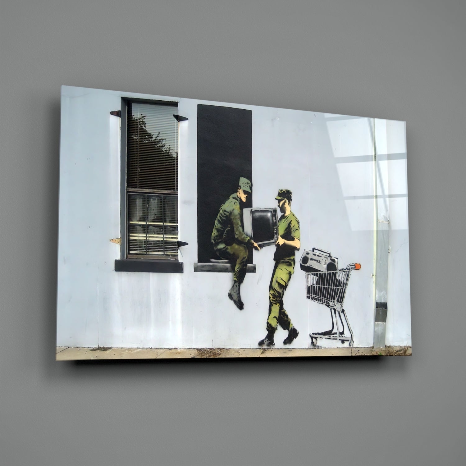 Glass art print depicting two olive-uniformed soldiers exchanging a television and shopping cart against white brick wall with windows.