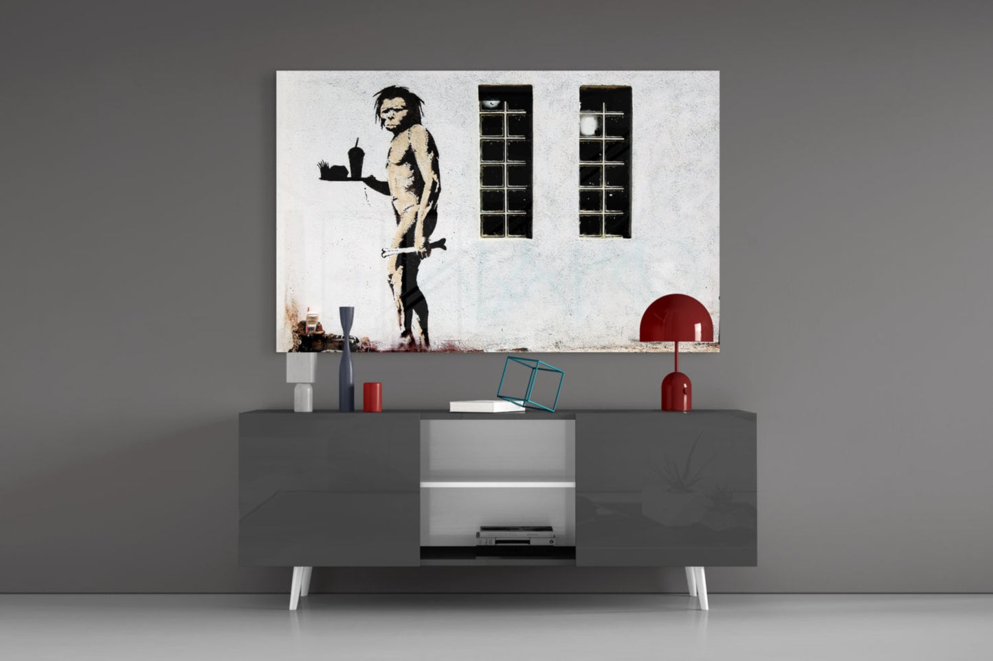 Neanderthal Glass Art print displayed above gray media console with red lamp and decorative objects in modern interior setting.