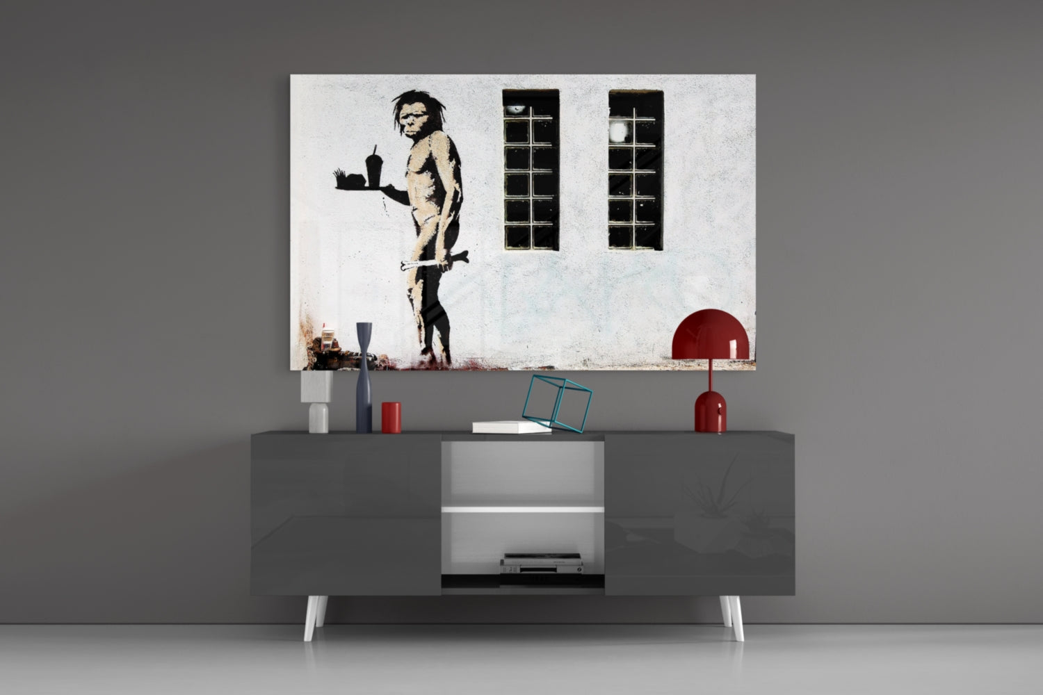 Neanderthal Glass Art print displayed above gray media console with red lamp and decorative objects in modern interior setting.