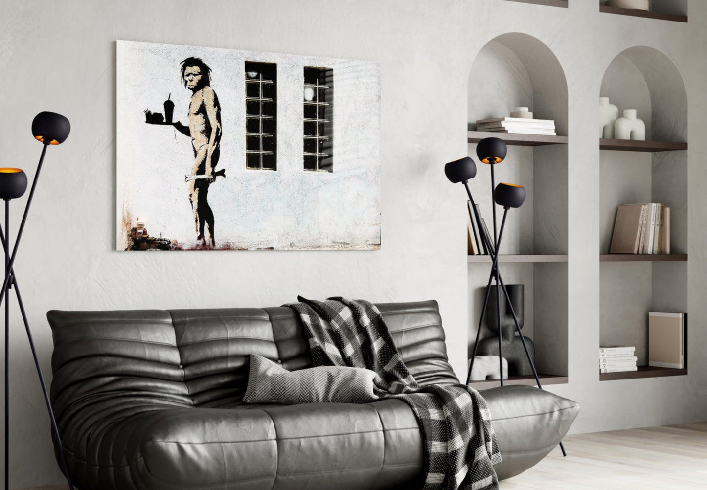 Black and white stencil artwork of a nude figure holding a tray, displayed above a gray leather sofa in a modern living room interior.