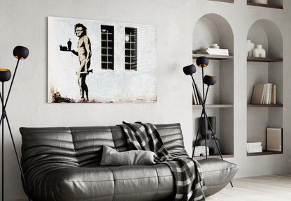 Black and white stencil artwork of a nude figure holding a tray, displayed above a gray leather sofa in a modern living room interior.