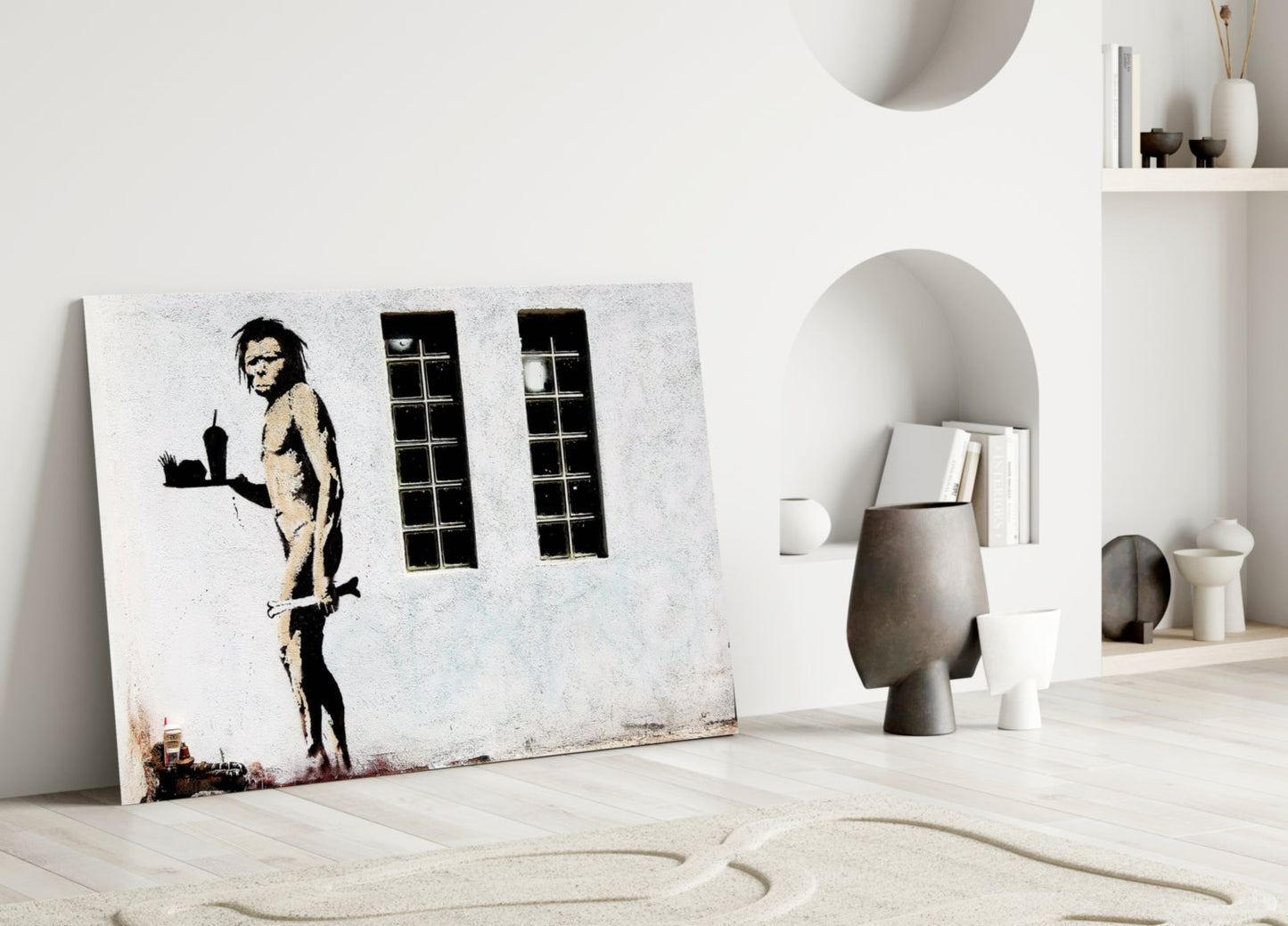 Street art canvas depicting a skeletal figure holding a cityscape, displayed in a minimalist white interior with decorative objects.