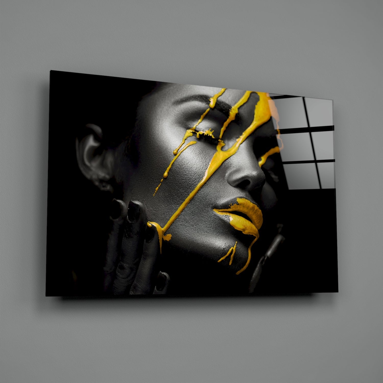 Monochrome portrait with yellow paint drips across face and lips, displayed on angled glass panel against gray wall.