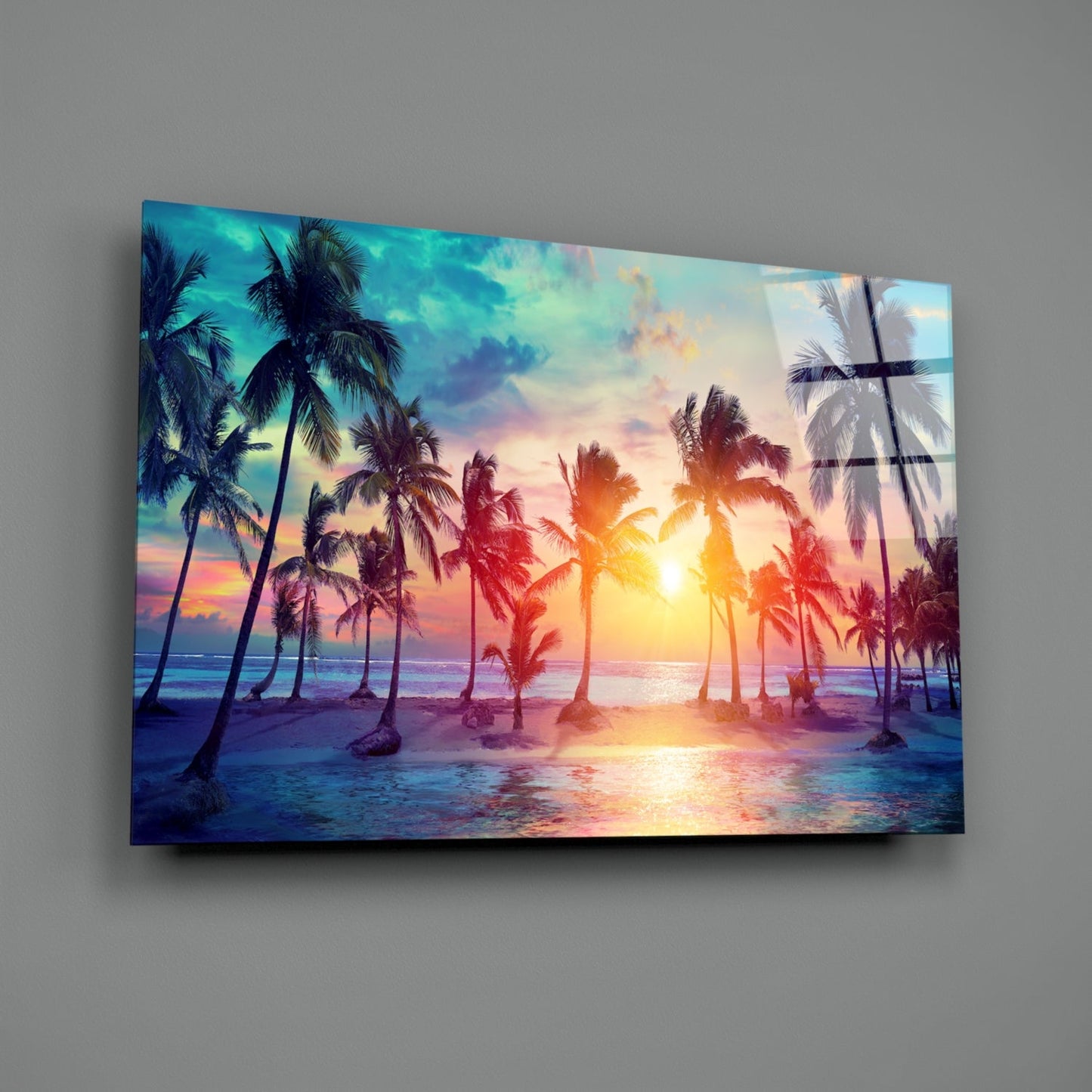 Glass art panel mounted on gray wall displaying tropical beach sunset with palm trees, golden sun, and colorful sky reflections.