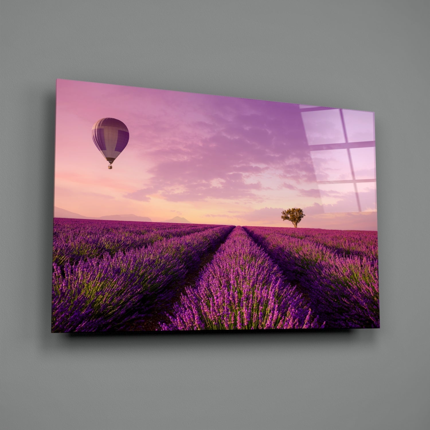 Glass art panel displaying lavender field at sunset with hot air balloon, mounted on gray wall at angle.