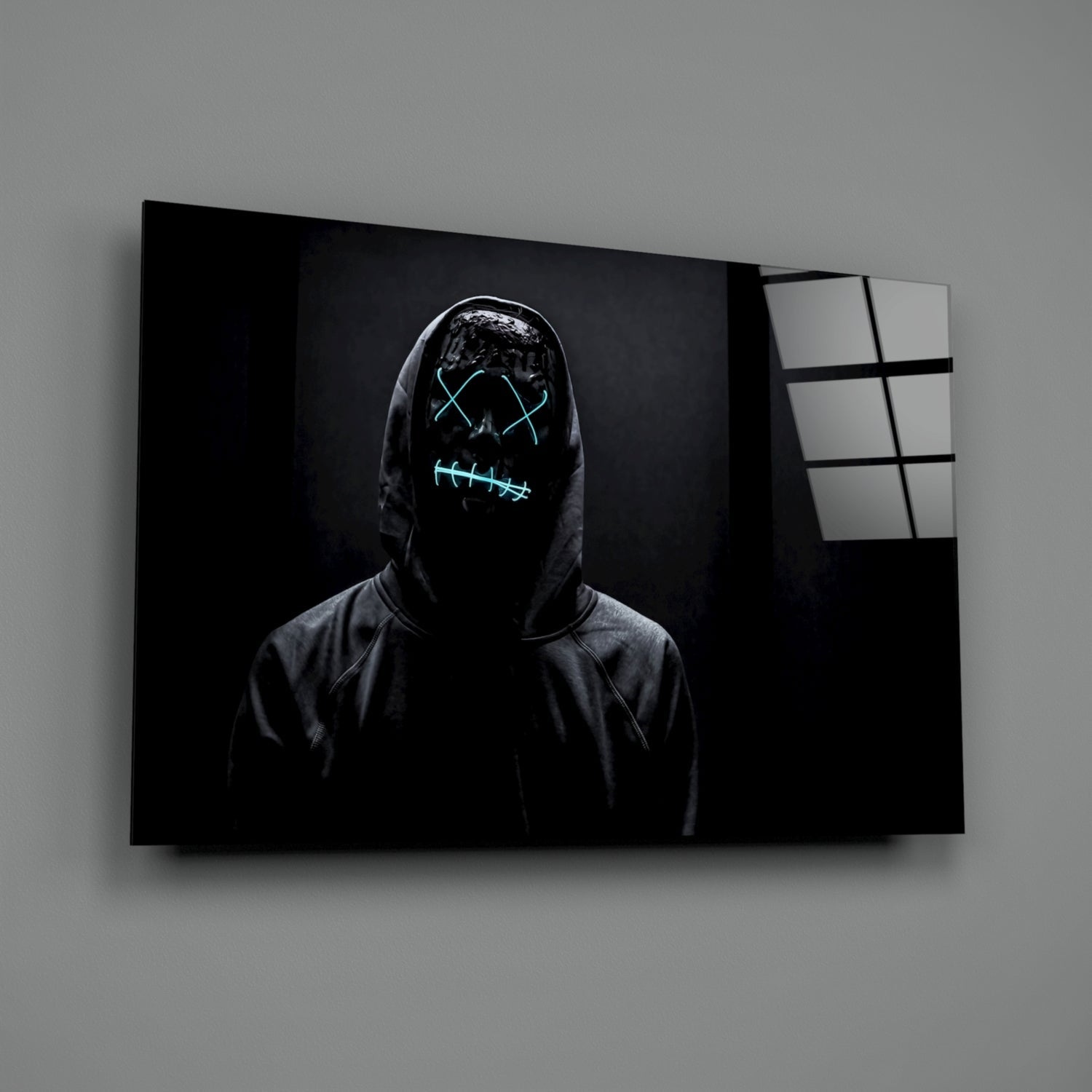 Figure in dark hoodie with neon cyan glowing mask design displayed on framed canvas against gray wall.