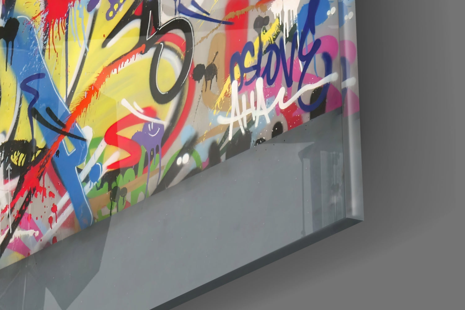 Angled view of colorful abstract graffiti-style glass art mounted on white wall, featuring bright yellow, red, blue, and pink spray-painted designs.