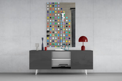 Artist on ladder installing colorful glass dots panel above gray media console in modern interior setting.