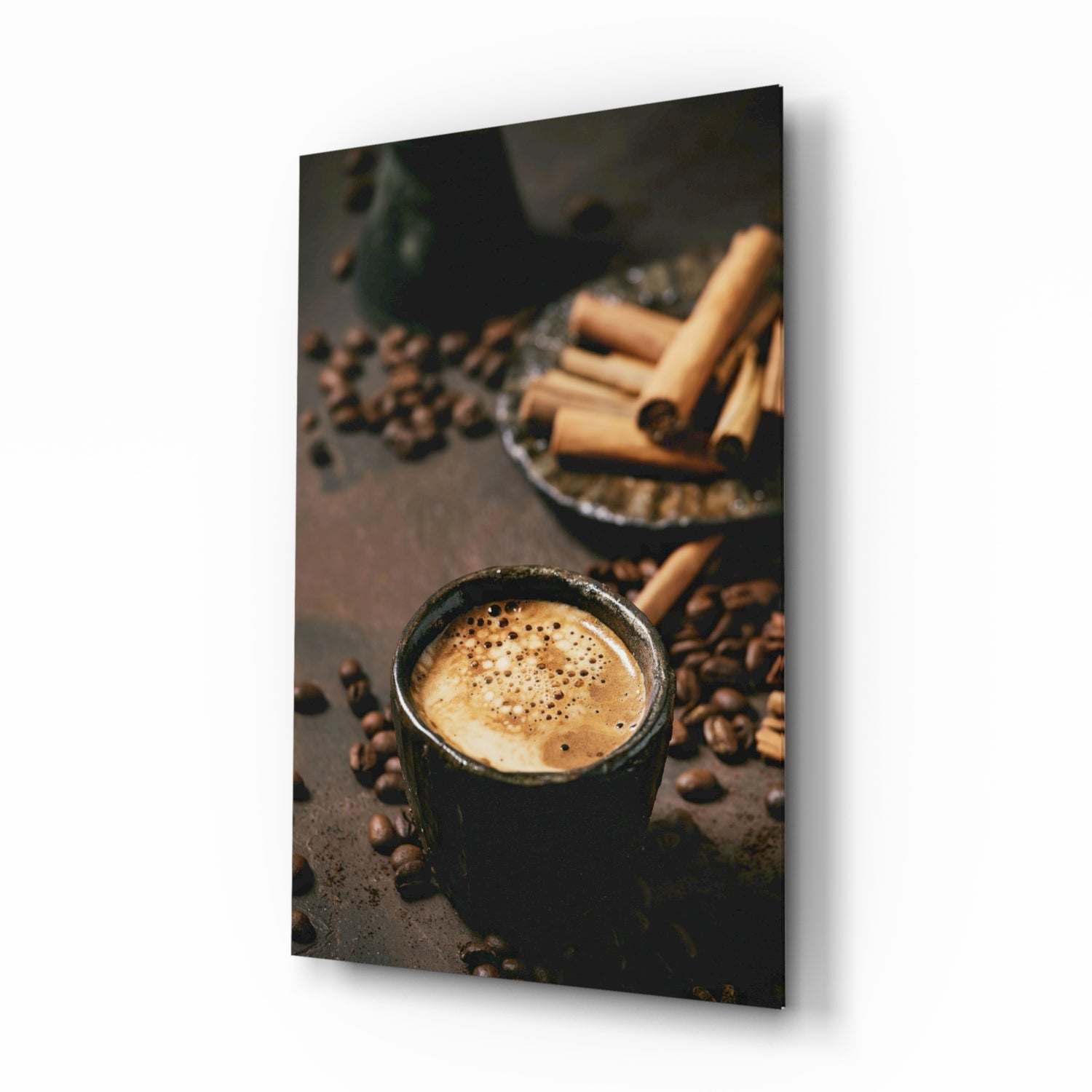 Black mug with cappuccino surrounded by coffee beans and cinnamon sticks on dark surface, displayed at angle.