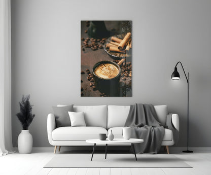 Dark ceramic mug filled with coffee and crema, surrounded by scattered coffee beans and cinnamon sticks on dark surface.