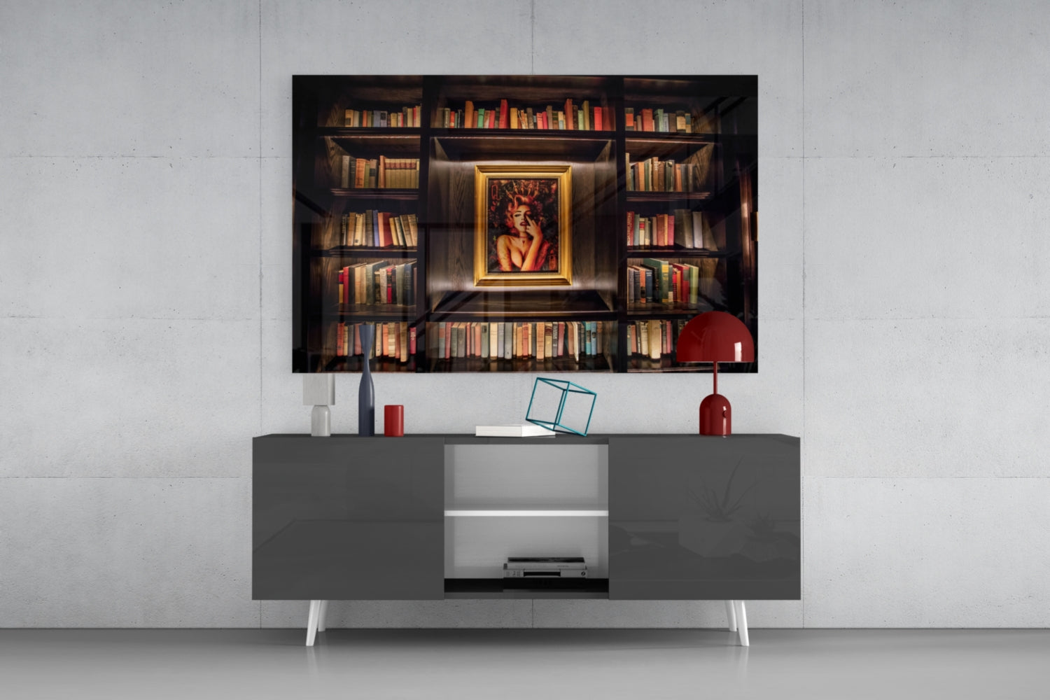 Framed glass art depicting an ornate bookshelf with gold-bordered portrait displayed above a modern gray media console with red accessories.