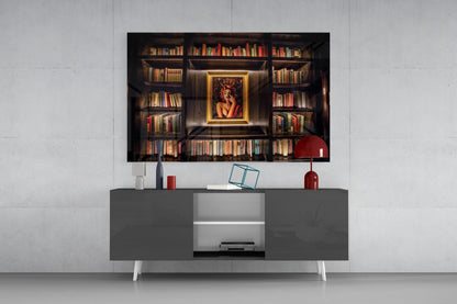 Framed glass art depicting an ornate bookshelf with gold-bordered portrait displayed above a modern gray media console with red accessories.