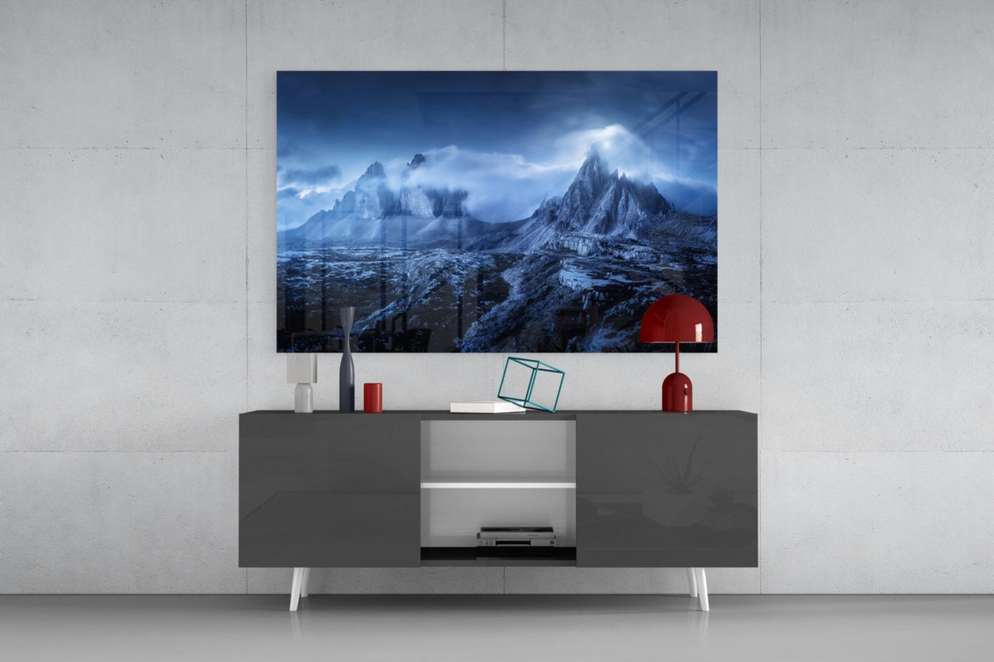 Mounted glass art depicting snow-covered mountains displayed above gray media console with red lamp and decorative accessories.