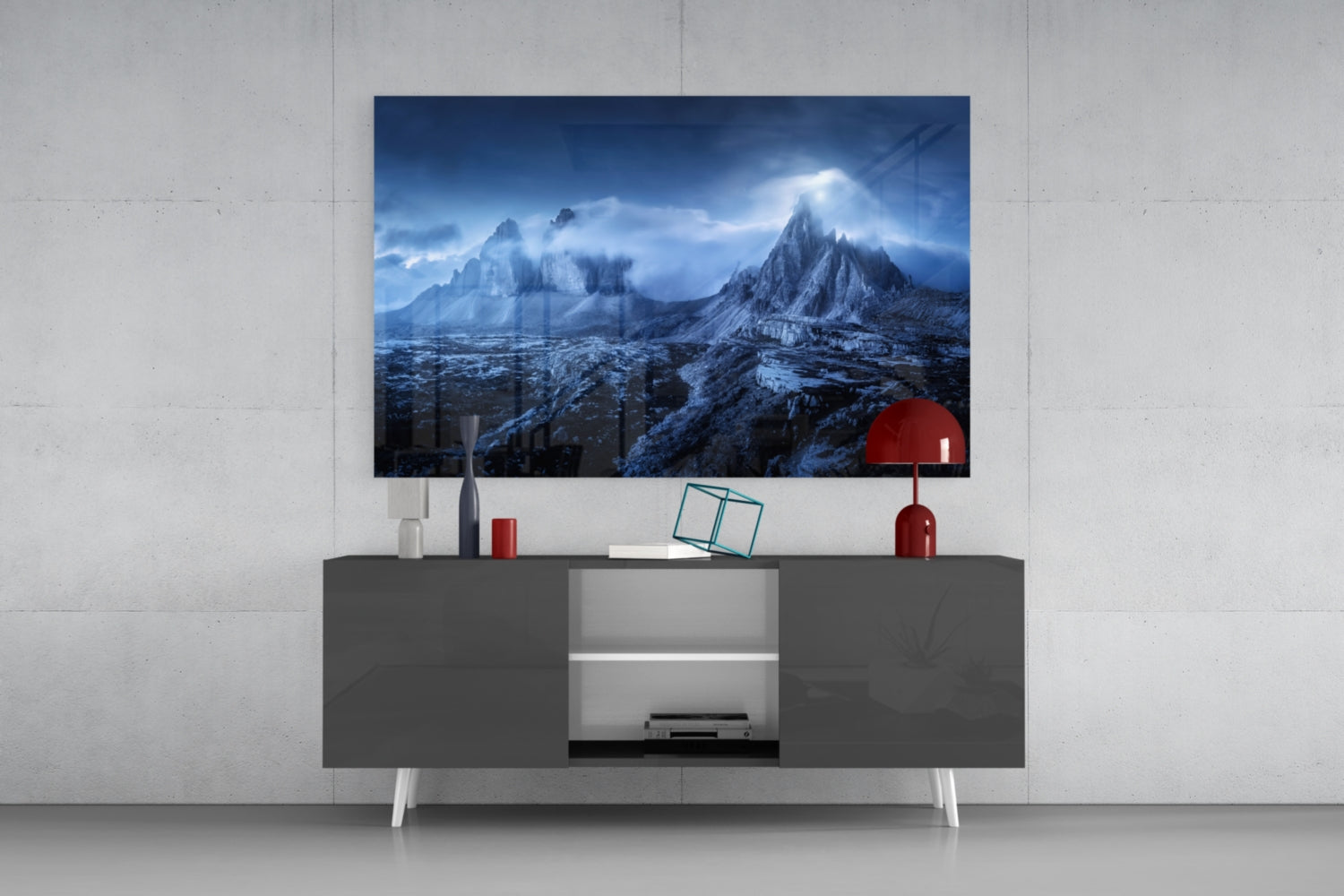 Mounted glass art depicting snow-covered mountains displayed above gray media console with red lamp and decorative accessories.