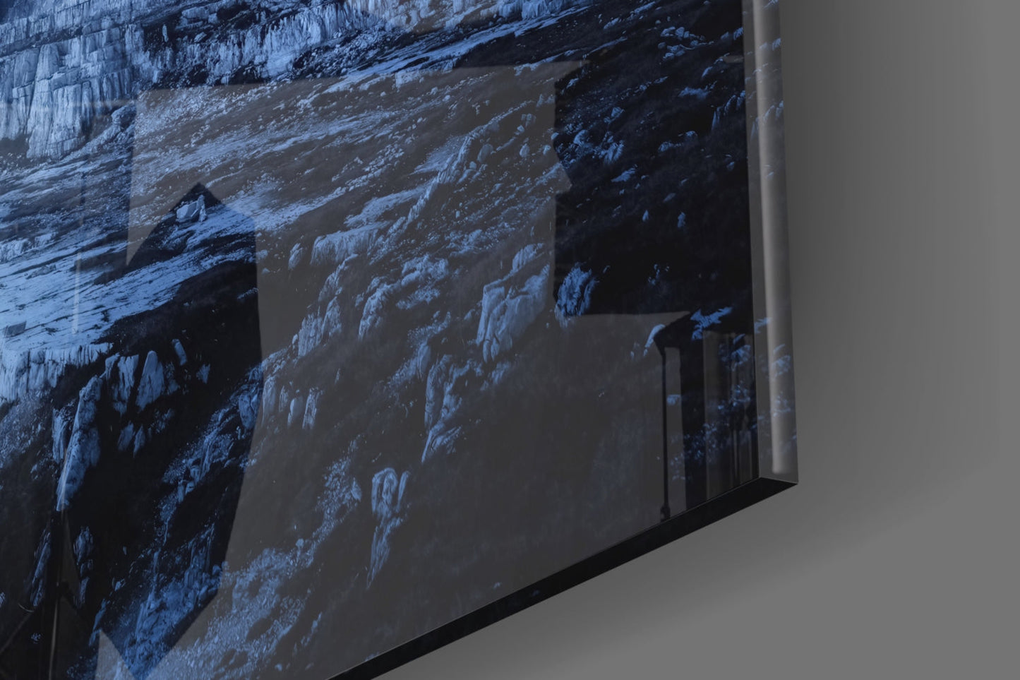 Side angle view of glass art panel displaying snow-covered mountain terrain in blue and white tones mounted on white wall.