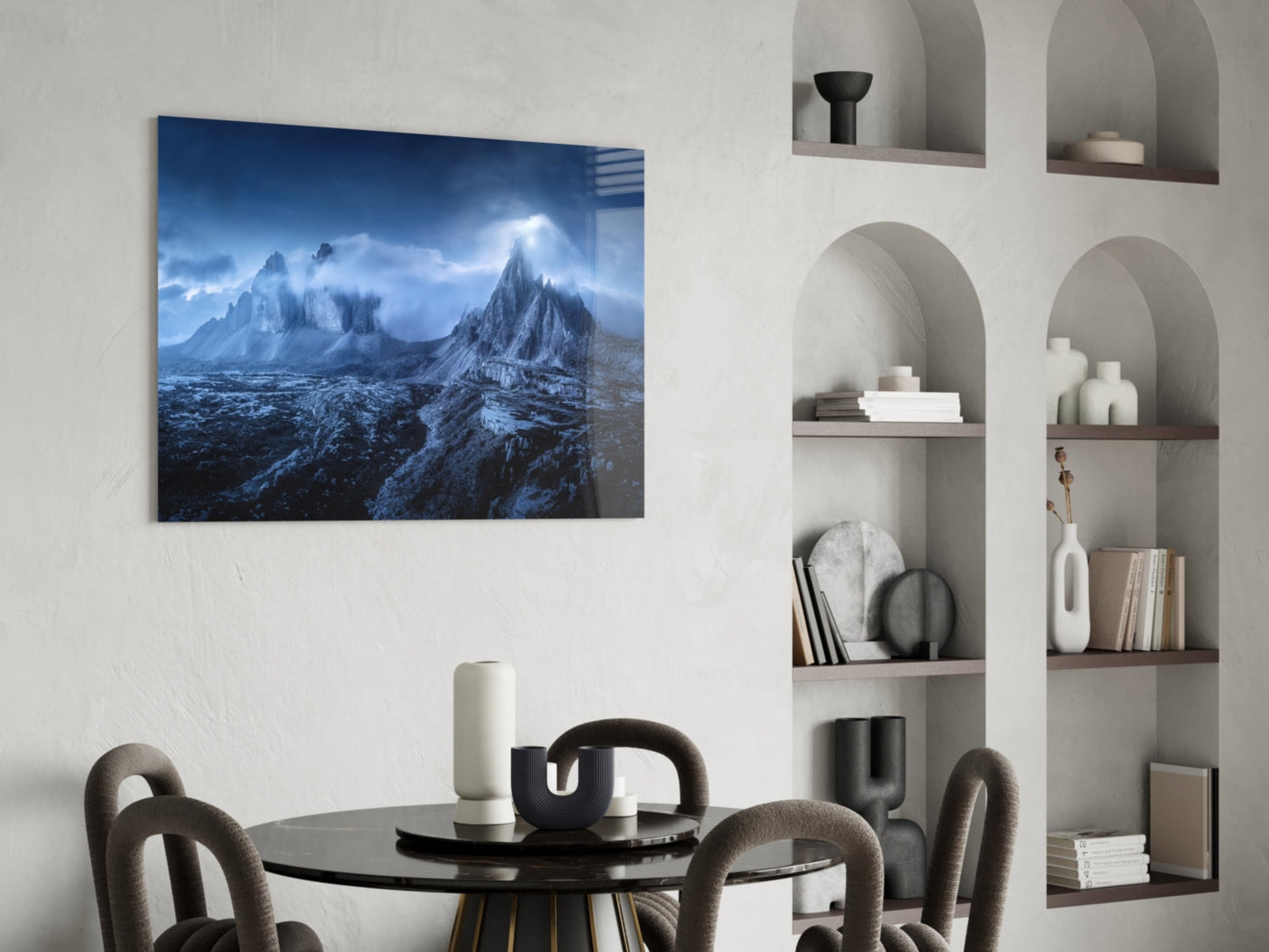 Blue-toned mountain landscape glass art hung above black dining table in minimalist white room with built-in shelving.