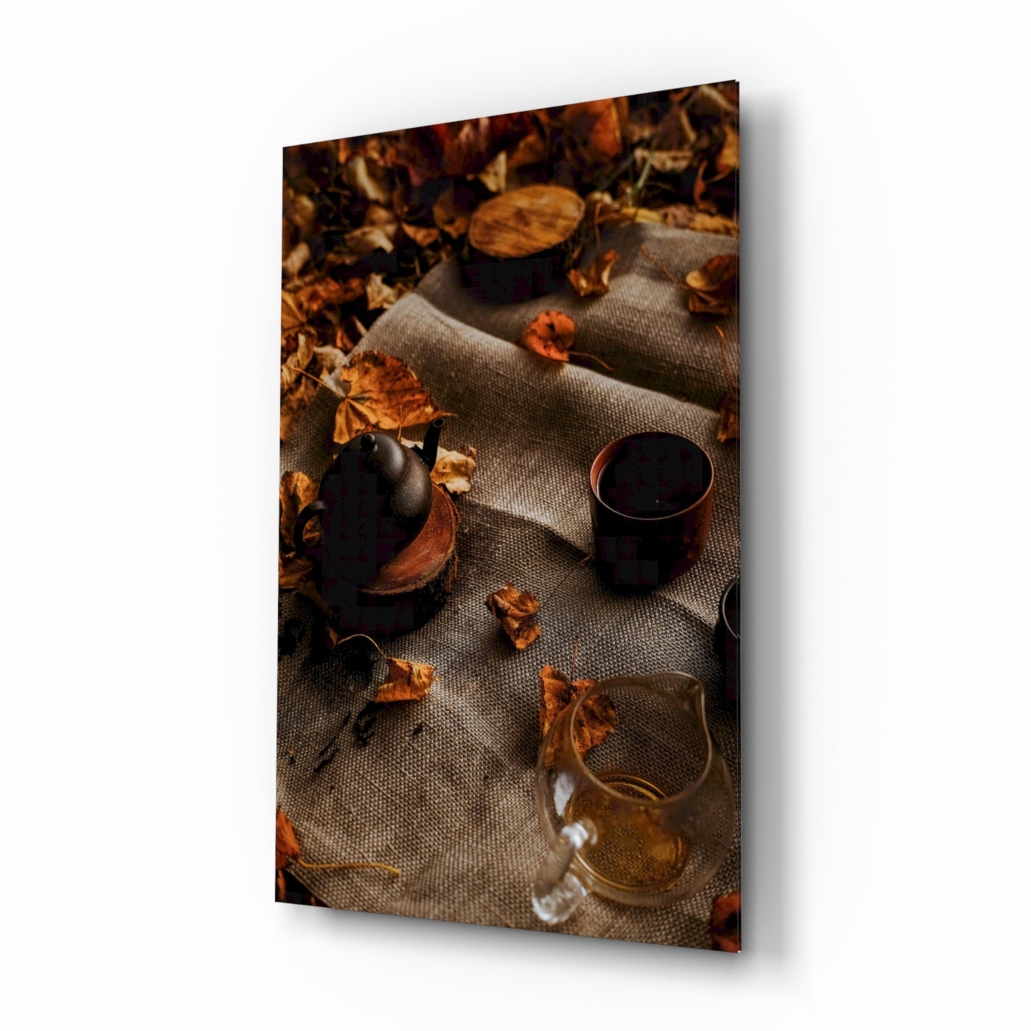 Overhead flat lay of autumn-themed glassware with dark beverages, dried leaves, and a gray linen cloth against warm lighting.
