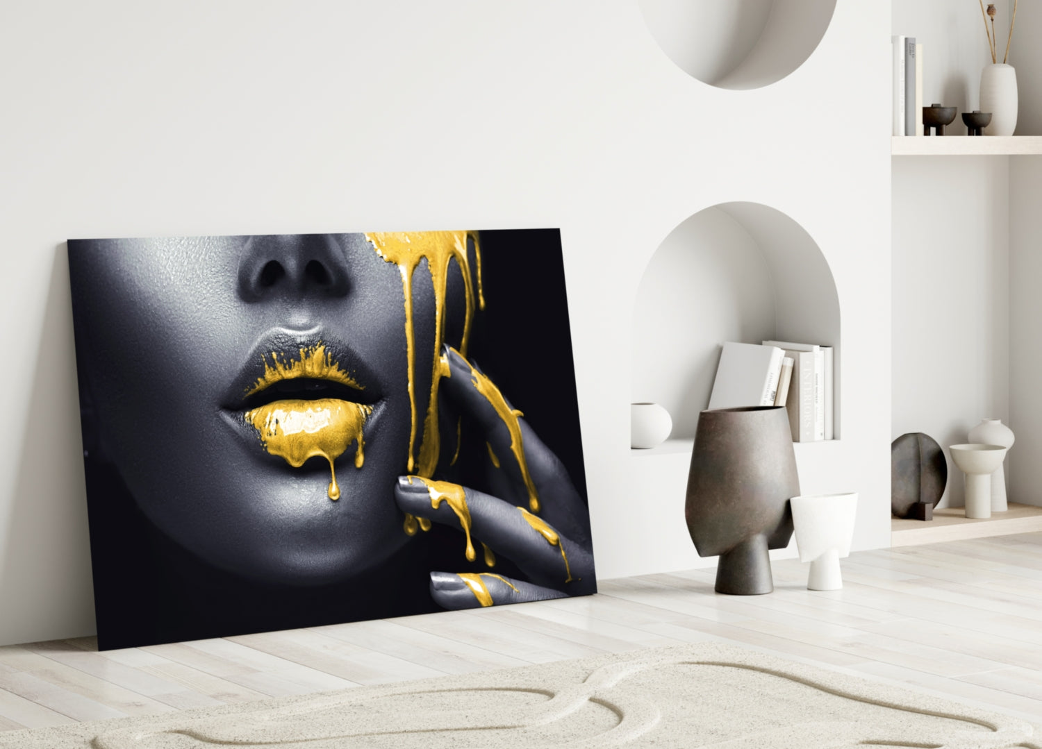 Glass wall art leaning against wall in minimalist interior, showing close-up of face with gold dripping lips on black background.